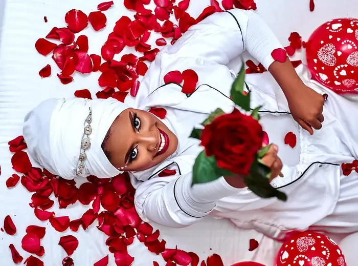 Tiffany lying among red rose petals holding a rose
